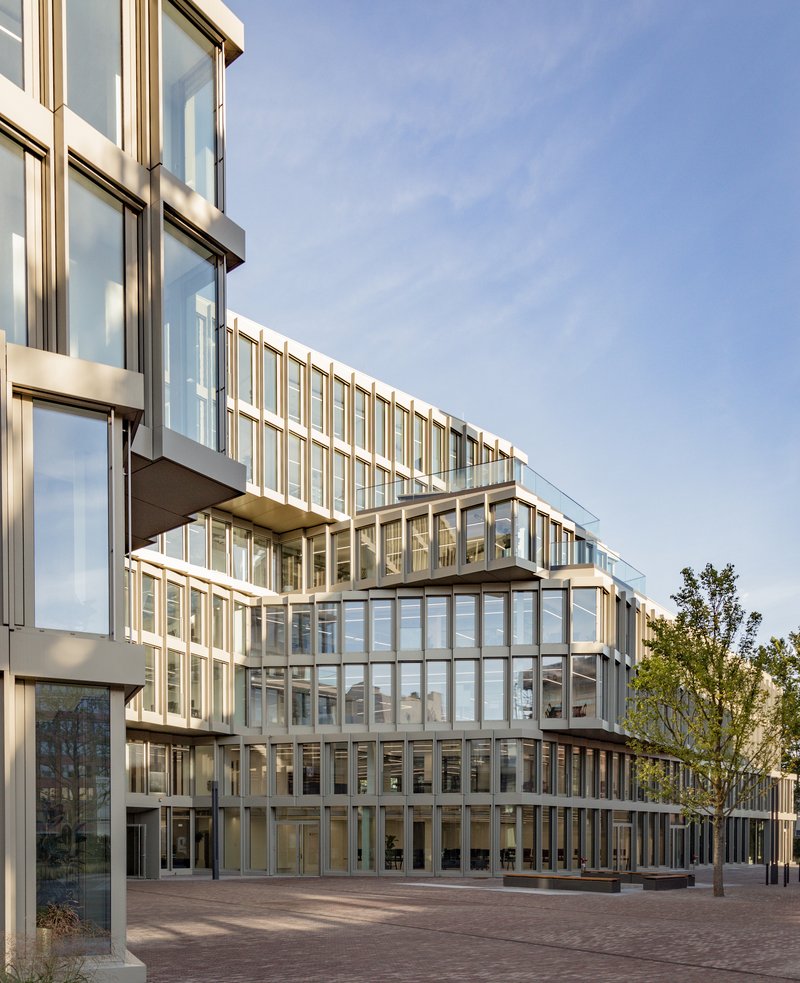 Courtyard view of the terraced glass and metal facade under afternoon light with trees