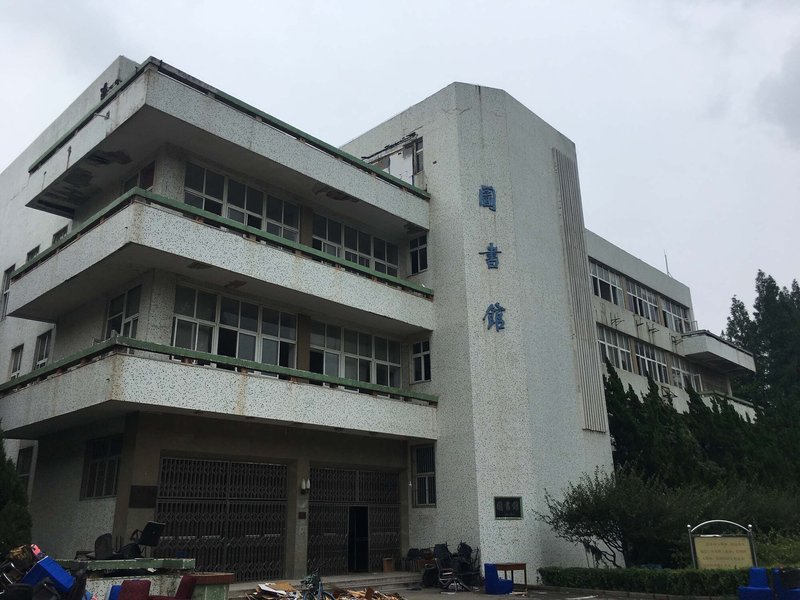 Three-story concrete facade with terrazzo cladding and vertically fluted tower element under overcast sky