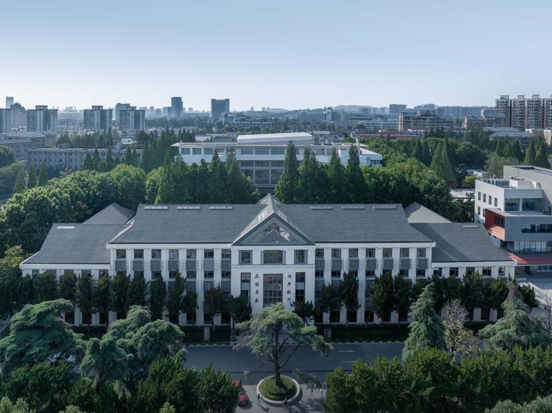 Aerial view of the white symmetrical facade with central pediment surrounded by dense green trees