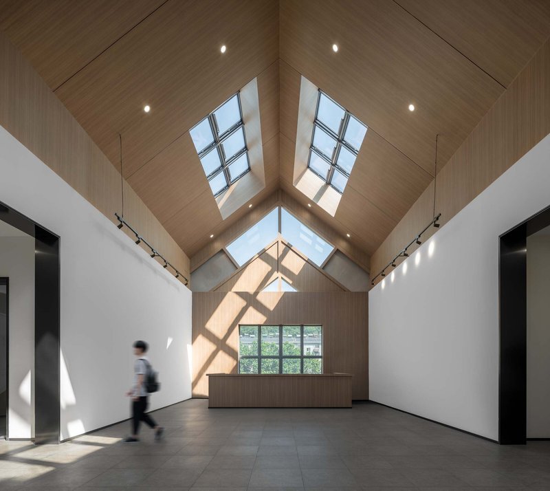 Vaulted gallery space with wood ceiling, skylight ridge and a figure passing through sunlight