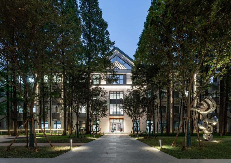 Front facade illuminated at dusk, framed by rows of tall trees along a paved walkway