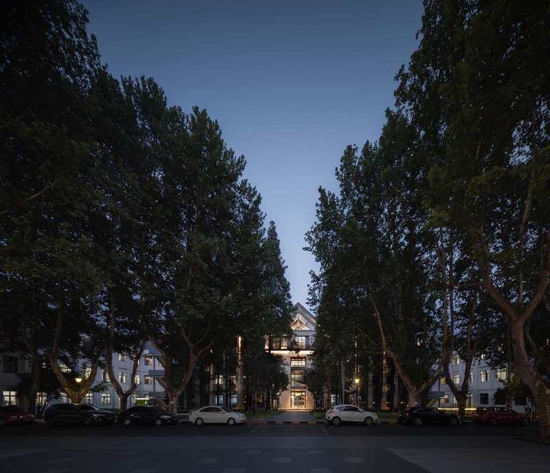 Illuminated central building framed by mature trees and parked cars in evening light