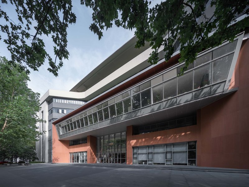 Curved facade with horizontal glazing bands and terracotta panels beneath overhanging tree branches