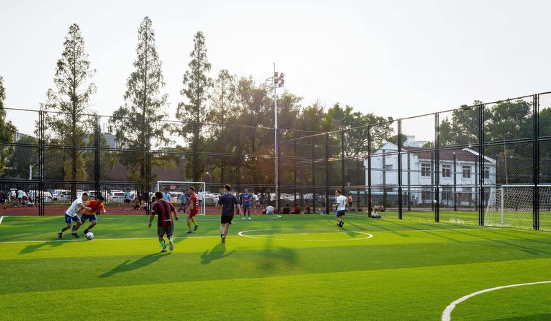 Synthetic turf sports pitch with mesh fencing and players in afternoon light
