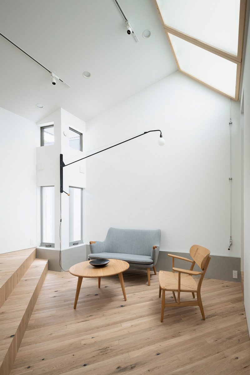 Double-height living room with timber-framed skylights and a grey sofa beneath tall windows