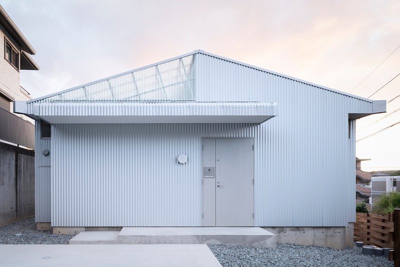 Street view of the white corrugated metal facade with a central door and translucent roof panels
