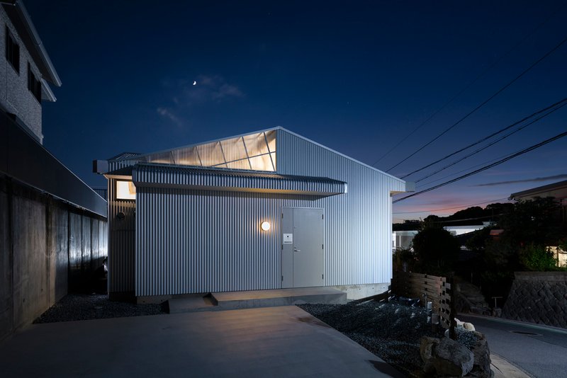 Street view of the vertical corrugated cladding and glowing clerestory windows under a crescent moon