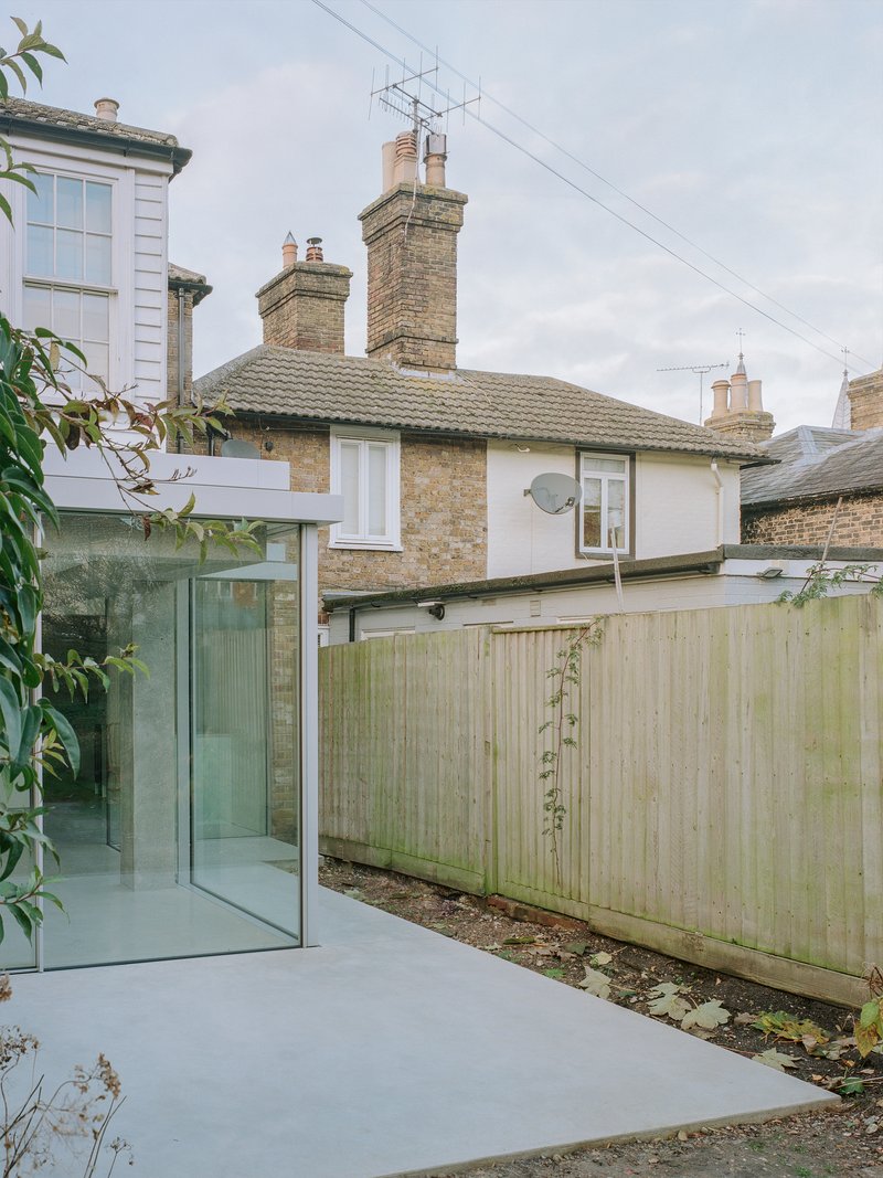 Rear extension with flat concrete roof and glazed corner beside weathered timber fence and existing brick houses