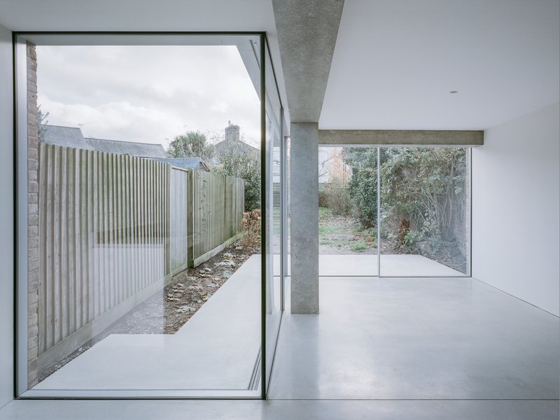White interior room with exposed concrete beam, cruciform column and sliding glass doors to garden courtyard