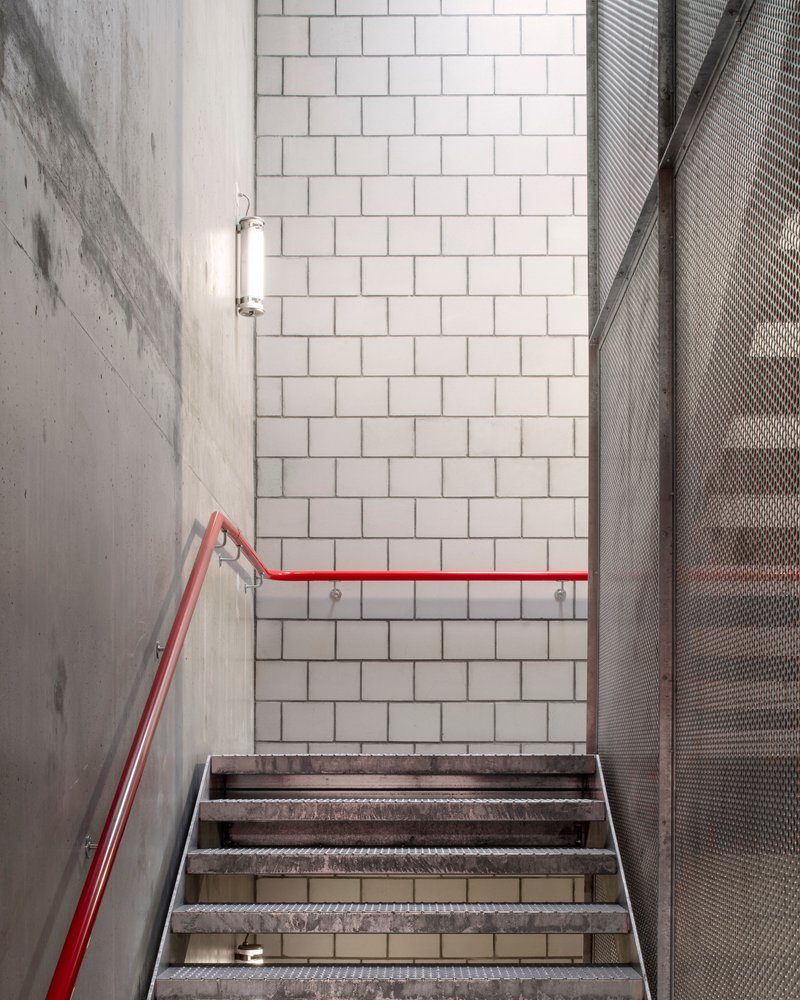 Concrete stairwell with red handrail, white tile wall and perforated metal screen panel