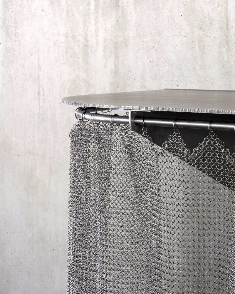 Close-up of chainmail curtain hanging from steel rod beneath a timber shelf edge