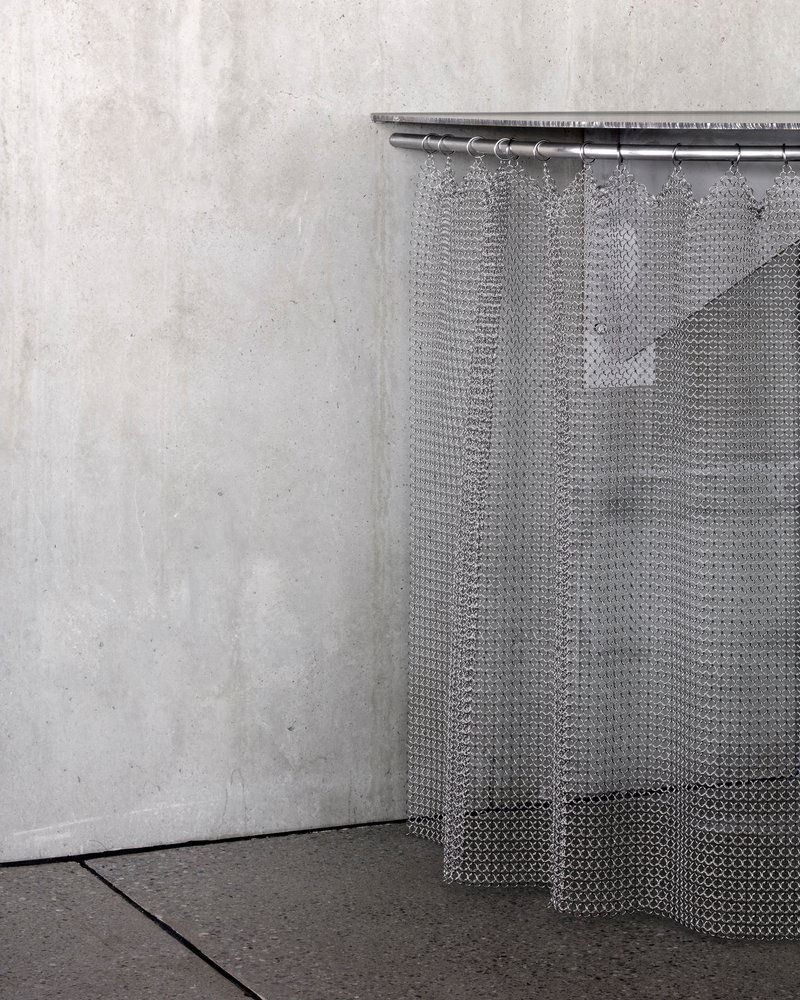 Metal mesh curtain suspended from rod in corner against poured concrete wall