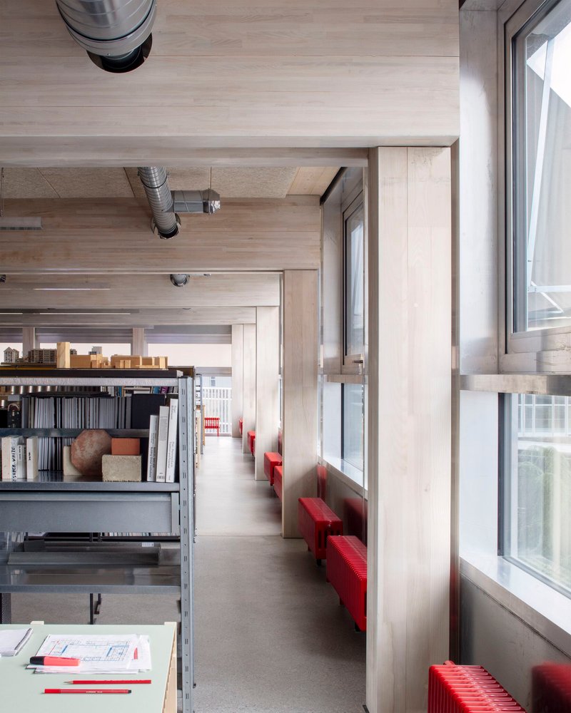 Corridor with timber-lined ceiling, red bench seating along windows, and metal shelving units
