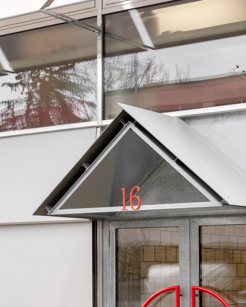 Triangular entry canopy with red numbering above glazed doors and recessed signage
