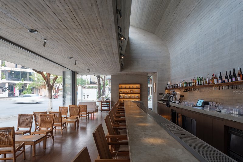 Interior of concrete bar space with timber ceiling and street-facing glazing at dusk