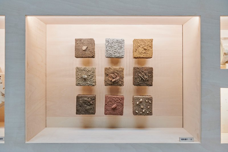 Nine textured earth and stone sample cubes arranged in a grid within a pale timber display box