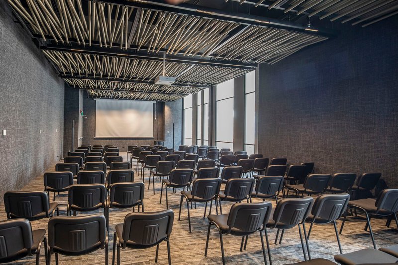Auditorium with rows of black chairs under an exposed steel and wood batten ceiling