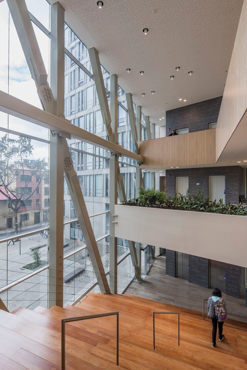 Interior atrium with diagonal white bracing members along the glazed curtain wall and planted upper balcony