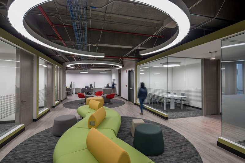 Open office lounge area with circular ceiling rings and modular seating as a person walks past