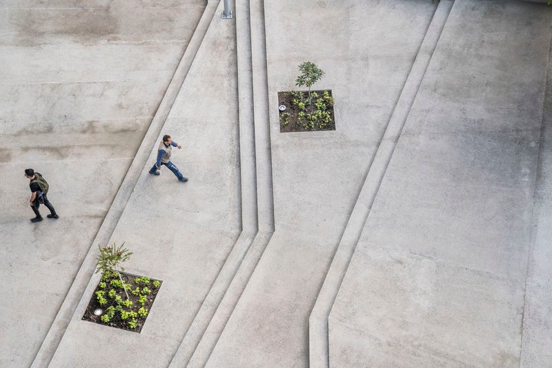Overhead view of the concrete plaza with angled relief channels and planted beds with two people walking