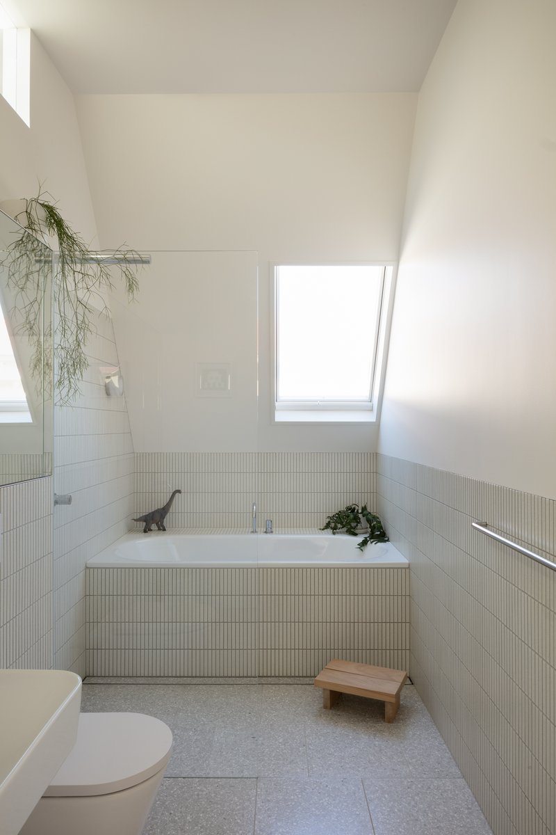 Bathroom with fluted tile wainscoting, built-in bathtub, and skylight above