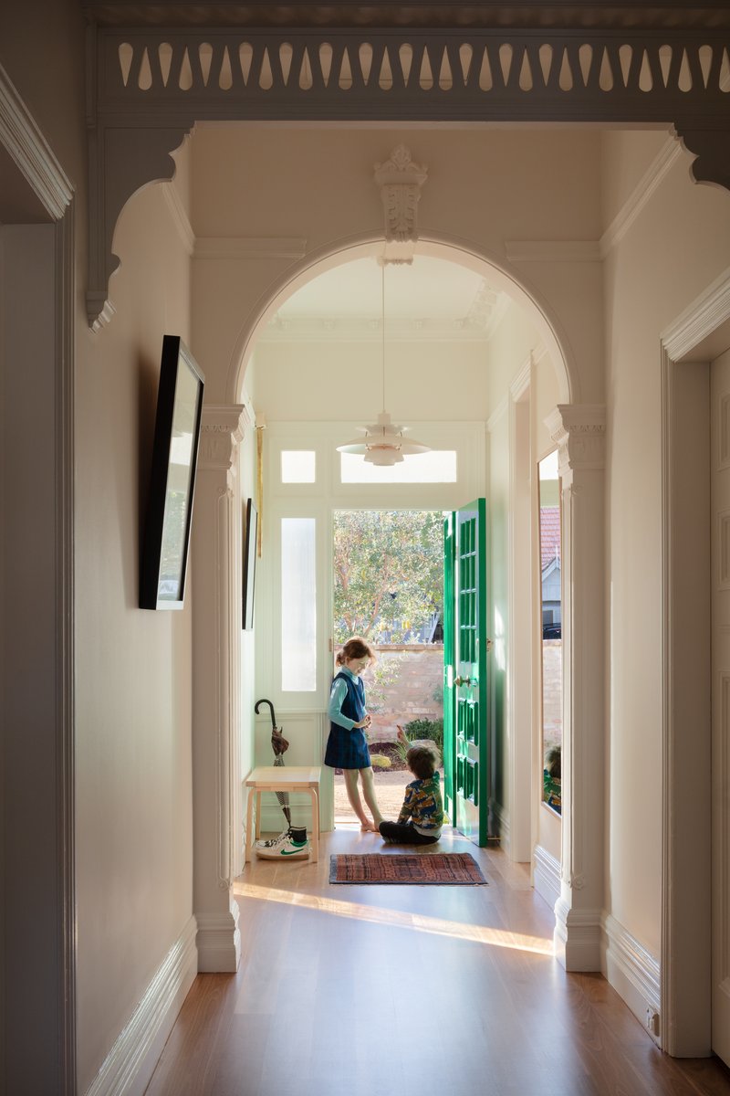 View through arched doorway and hallway toward bright green entry door with two children inside