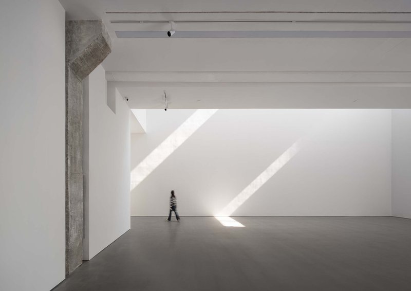 Gallery hall with raw concrete column and figure walking through diagonal sunlight on floor