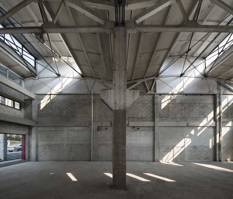 Exposed concrete structure with central column and steel roof trusses in bright natural light