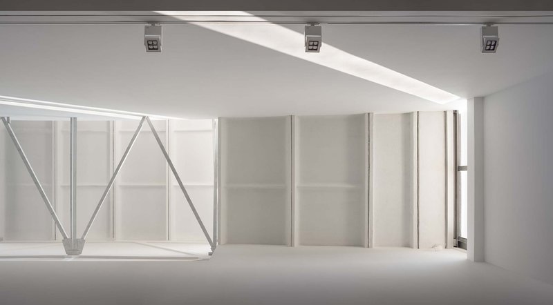 Gallery space with exposed steel truss structure and white partition walls below a clerestory