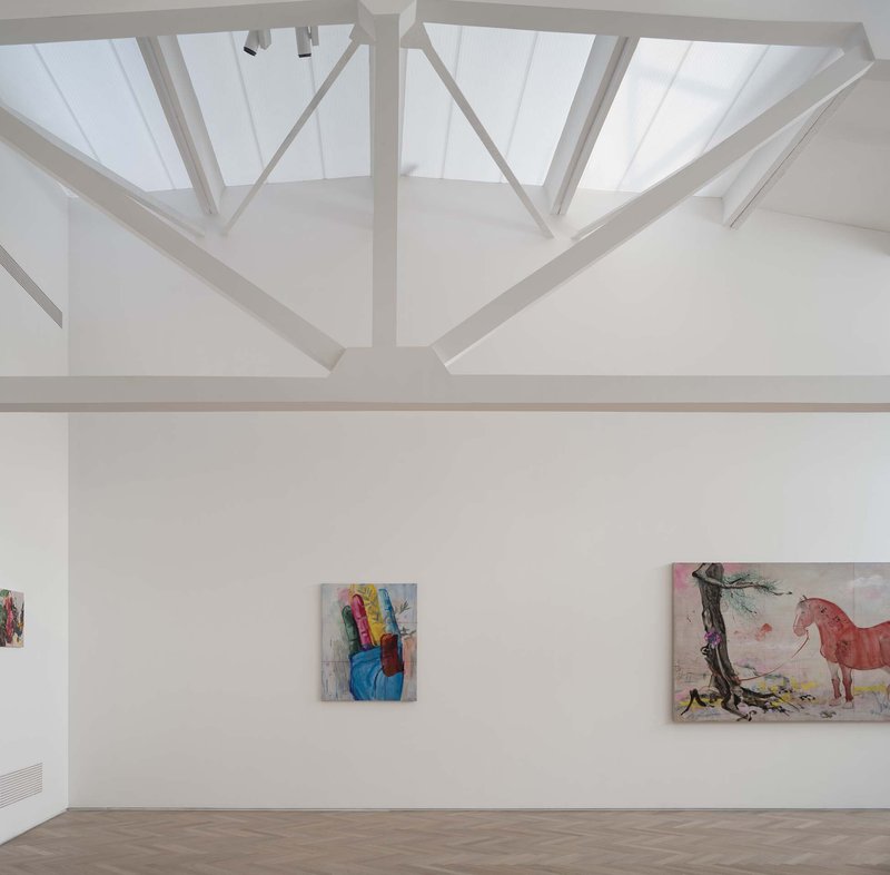 Interior gallery with exposed steel roof trusses and skylights above paintings on white walls
