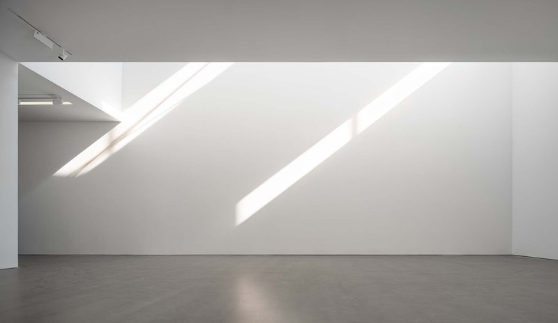 Gallery corner with diagonal skylights casting parallel bands of sunlight on the white wall