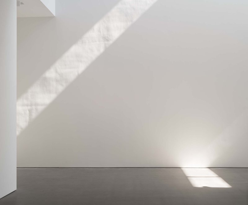 White interior corner with diagonal shadows cast by unseen skylight above grey concrete floor