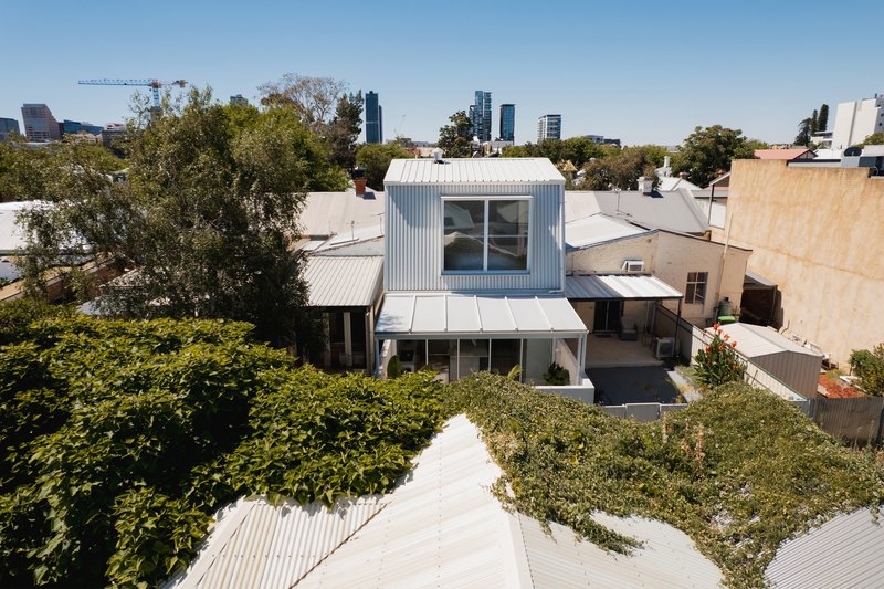 Aerial view of the white corrugated rooftop volume surrounded by mature trees and neighboring roofs