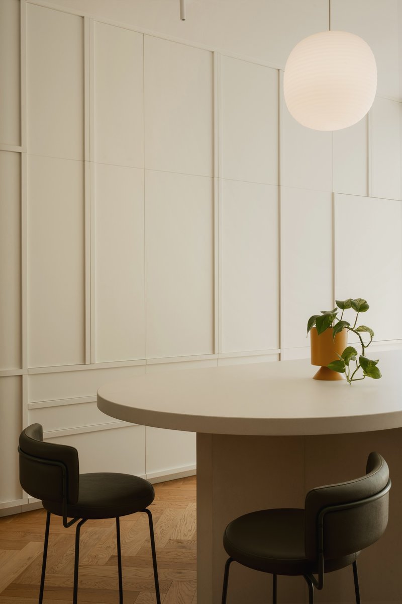 Round dining table with dark upholstered chairs and potted plant under spherical pendant at dusk