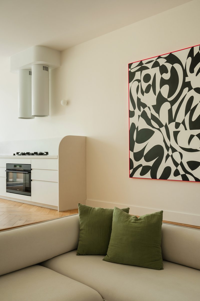 Living space with open kitchen and abstract artwork above sofa with green cushions