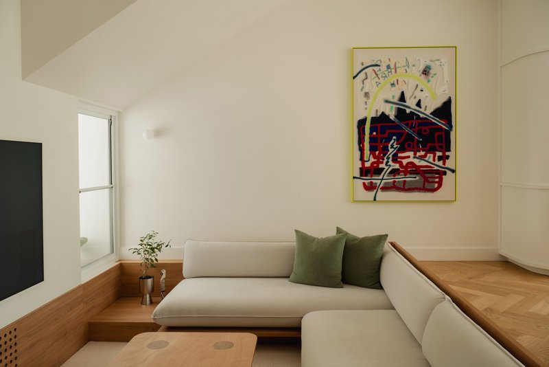 Corner sofa with integrated timber platform and colorful framed artwork on wall
