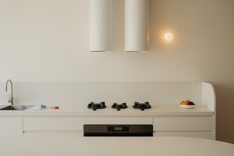Minimalist kitchen with white countertop, three gas burners, and cylindrical range hood under warm evening light