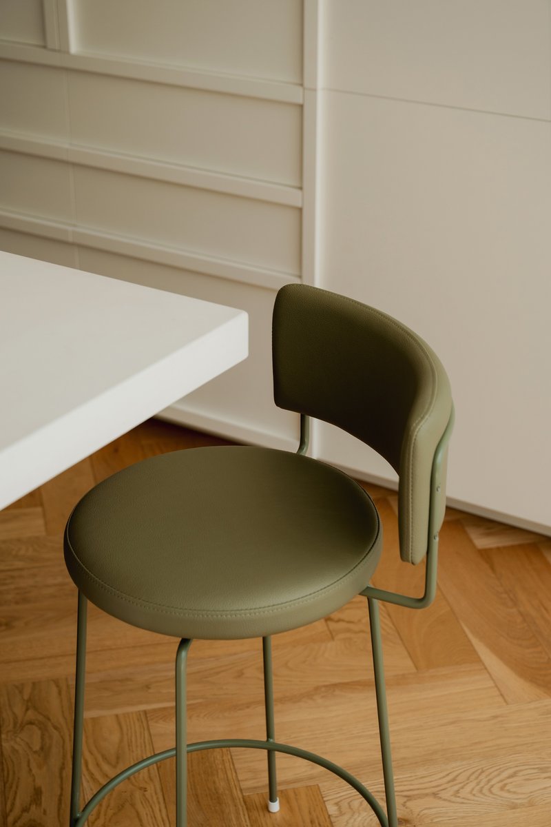 Olive green upholstered chair with curved backrest tucked beneath a white table on herringbone timber floor