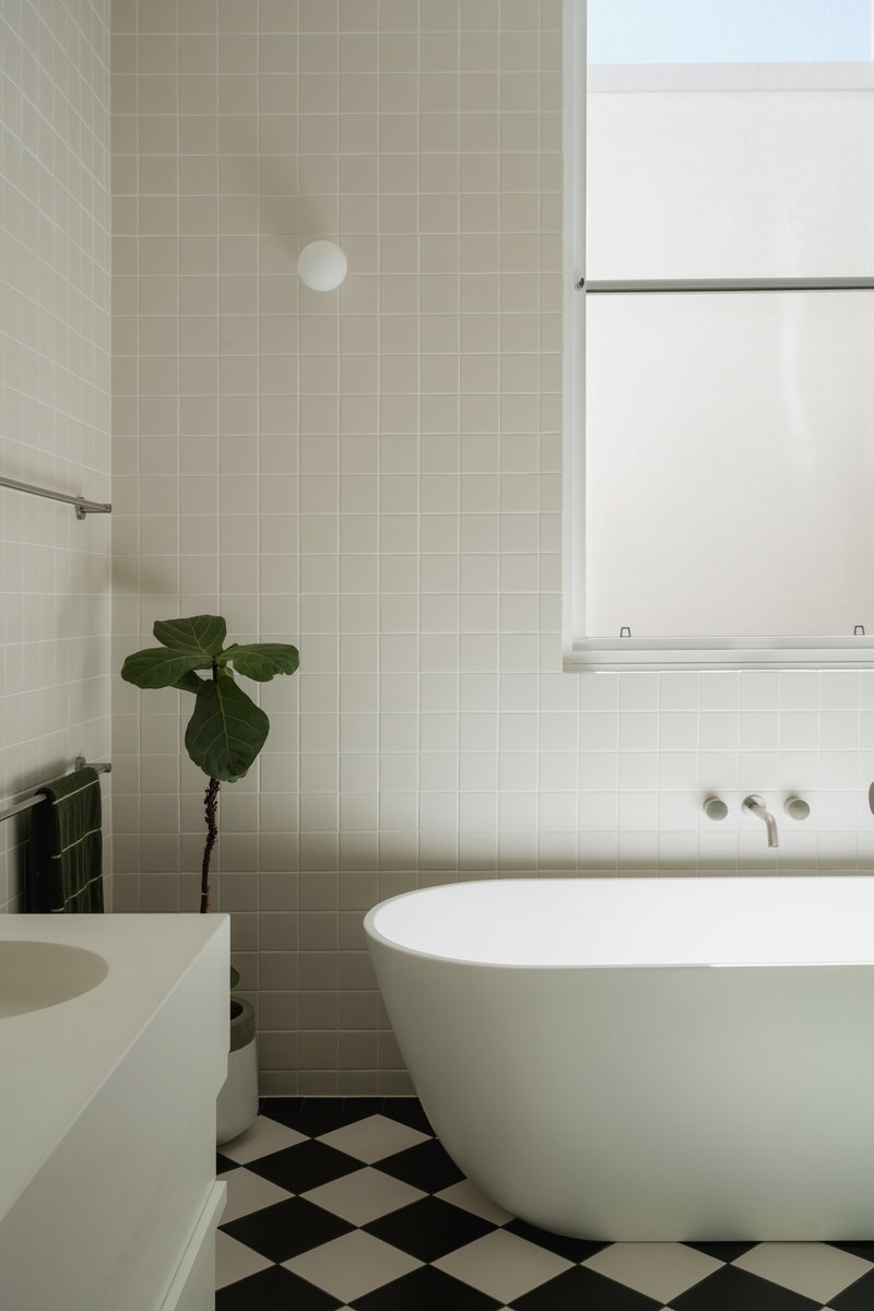 Bathroom with freestanding tub, checkerboard floor tiles, and square mosaic wall tiles beside a window