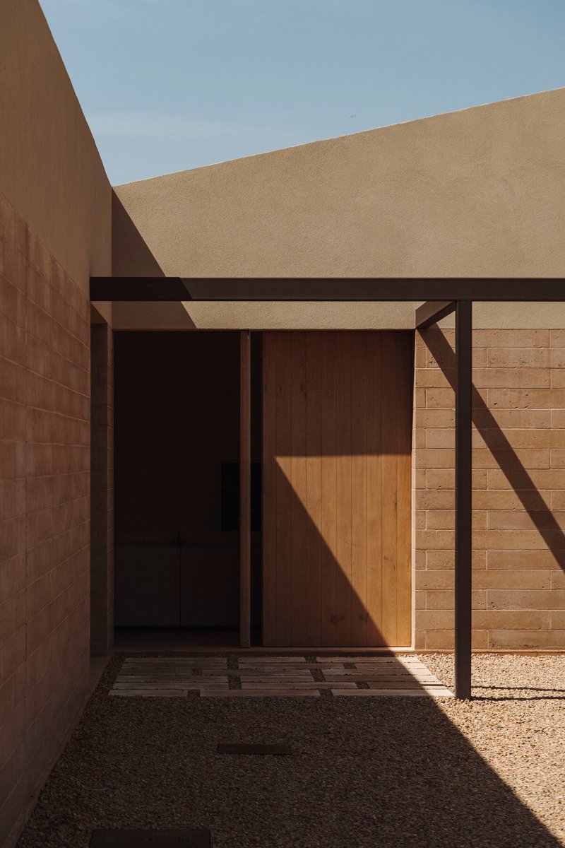 Entry portal with steel frame and timber door caught in afternoon light within courtyard walls