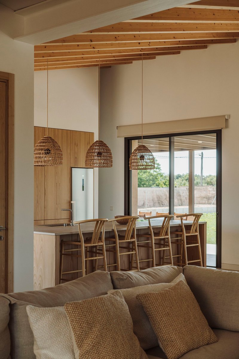 Open-plan living area with exposed timber ceiling beams and kitchen island beneath woven pendant lights
