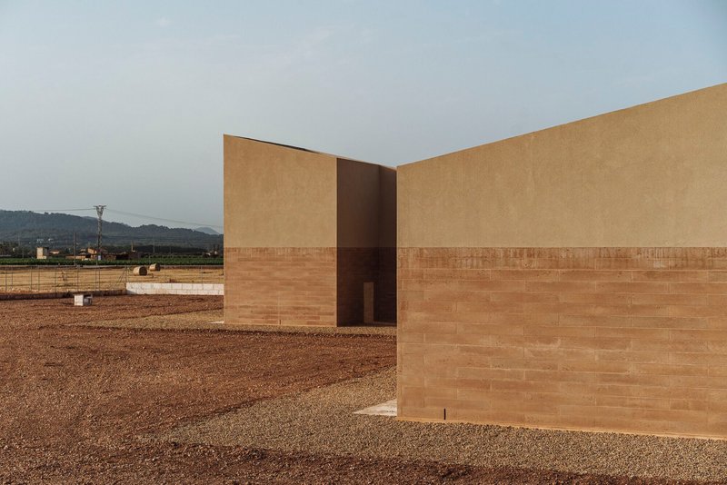 Corner detail of the two-tone facade with rammed earth base and stucco upper volume