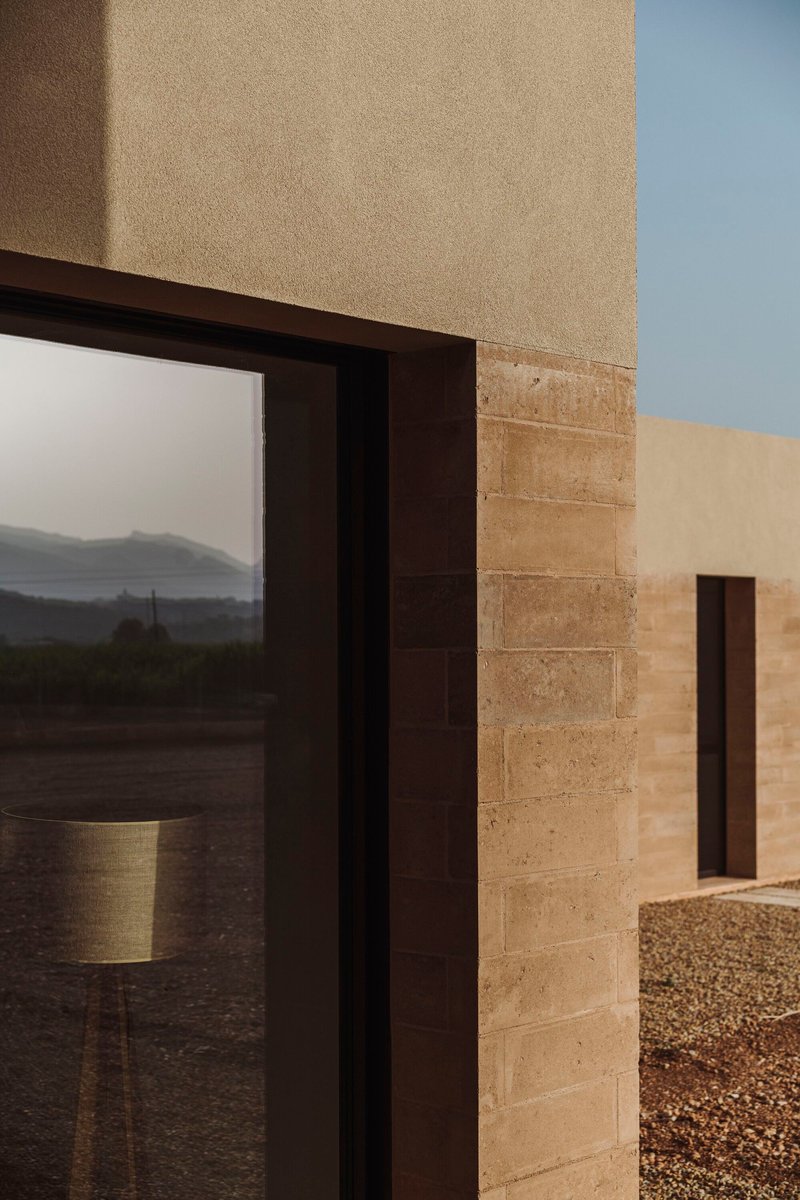 Corner detail of stacked stone masonry meeting a dark metal window frame at dusk