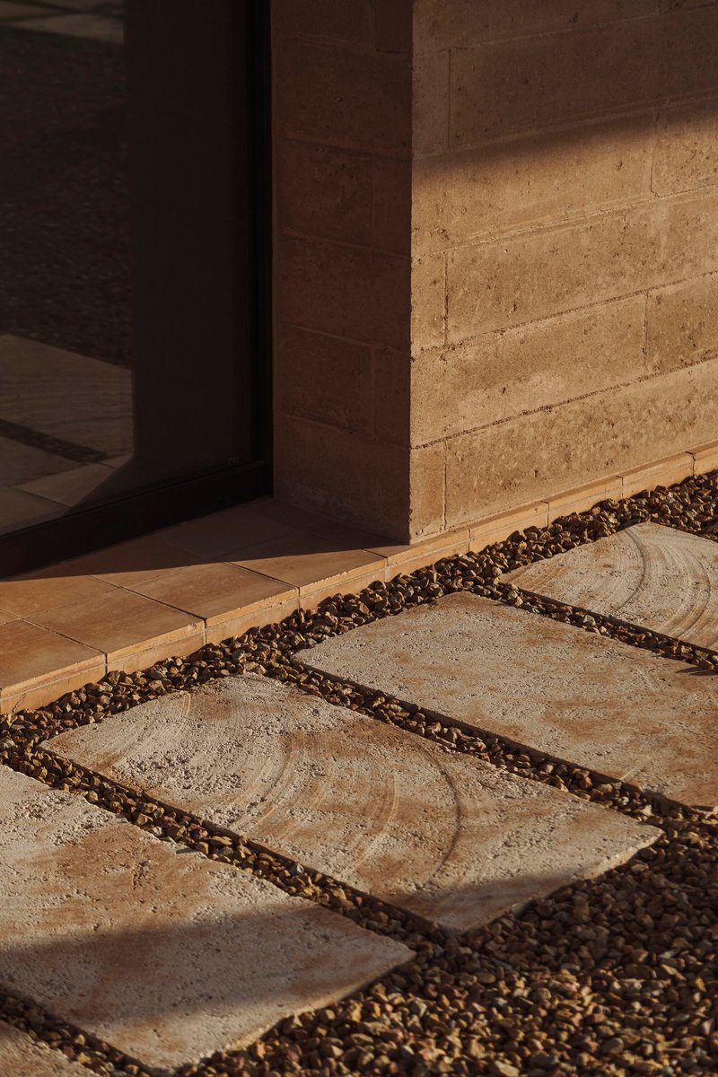Stone pavers set in gravel leading to a doorway with rammed earth wall in sunlight