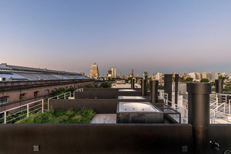 Rooftop terrace with planted beds and cylindrical metal ventilation towers under an evening sky