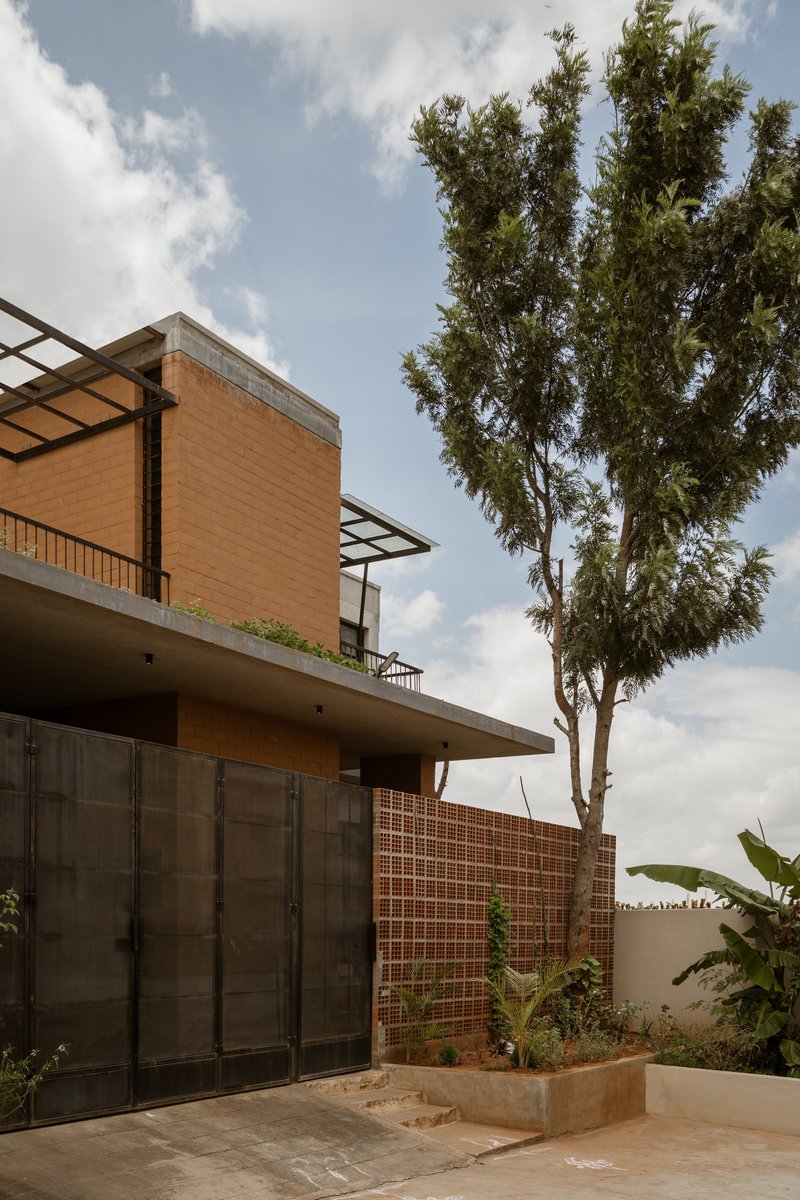 Courtyard view showing stacked volumes with perforated brick screen and cantilevered canopy beside a tall tree