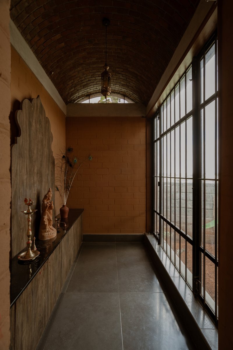 Corridor with gridded steel-frame door opening to landscape beneath a curved brick ceiling vault