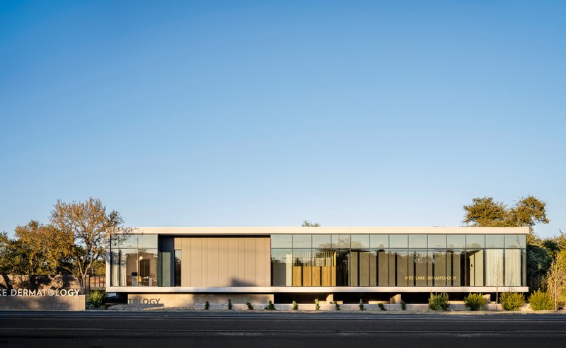 Street-facing facade with vertical metal panels and floor-to-ceiling glass flanked by trees in afternoon light