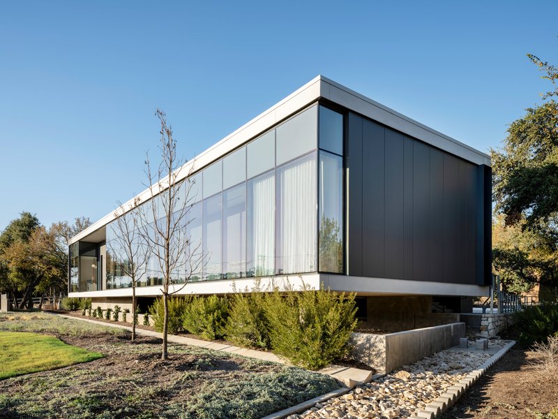 Corner view showing the cantilevered dark metal cladding above a planted slope with young trees
