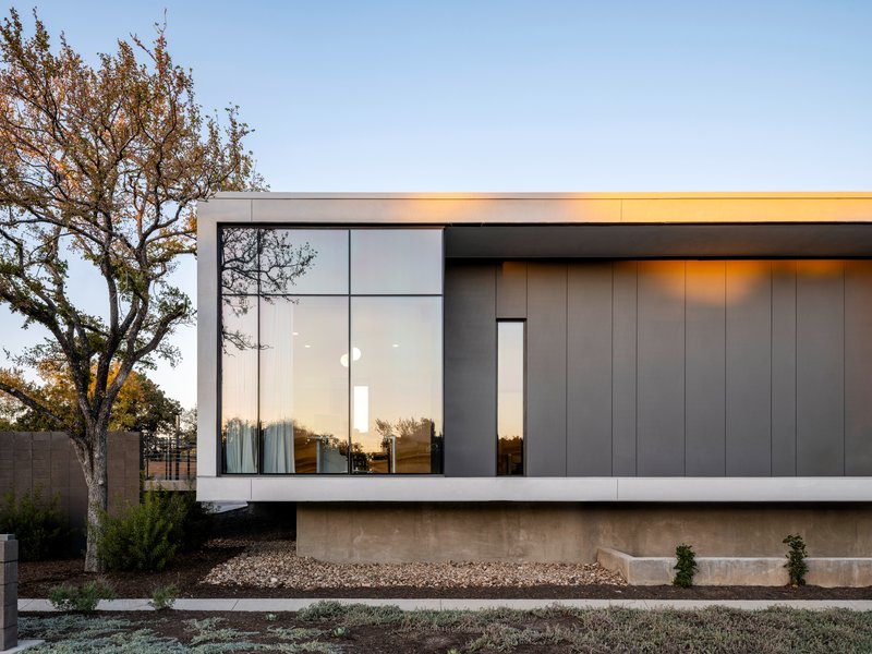 Facade detail of the vertical metal panels meeting the glazed corner beneath a flat roof overhang